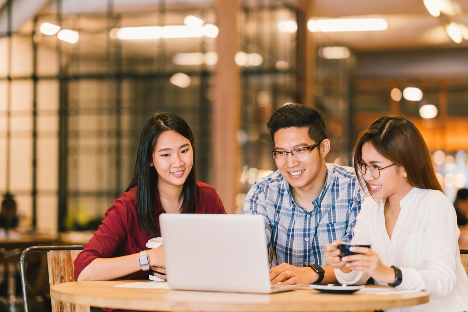 Three young adults happily working together on a laptop in a cozy café.